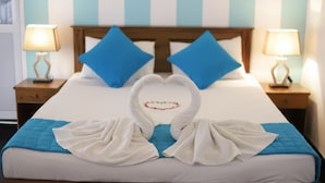 Une chambre d’hôtel avec un lit, deux tables de chevet, une décoration en forme de cœur réalisée avec des serviettes et des motifs rayés sur les murs.