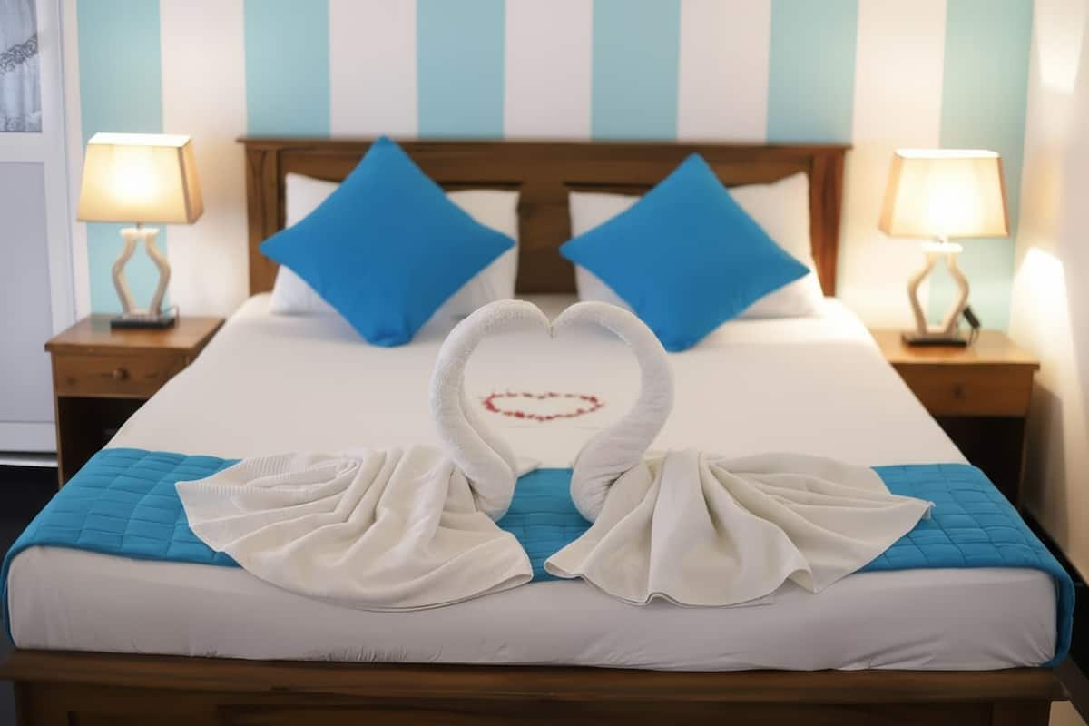 Habitación de hotel con cama, dos mesitas de noche, una decoración de toallas en forma de corazón y detalles decorativos en la pared a rayas.
