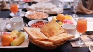 Une table mise pour le petit-déjeuner avec des tartines, des fruits et du jus d’orange.