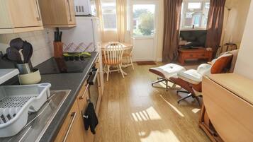 Cocina compacta con comedor, televisor y ventana con cortinas.