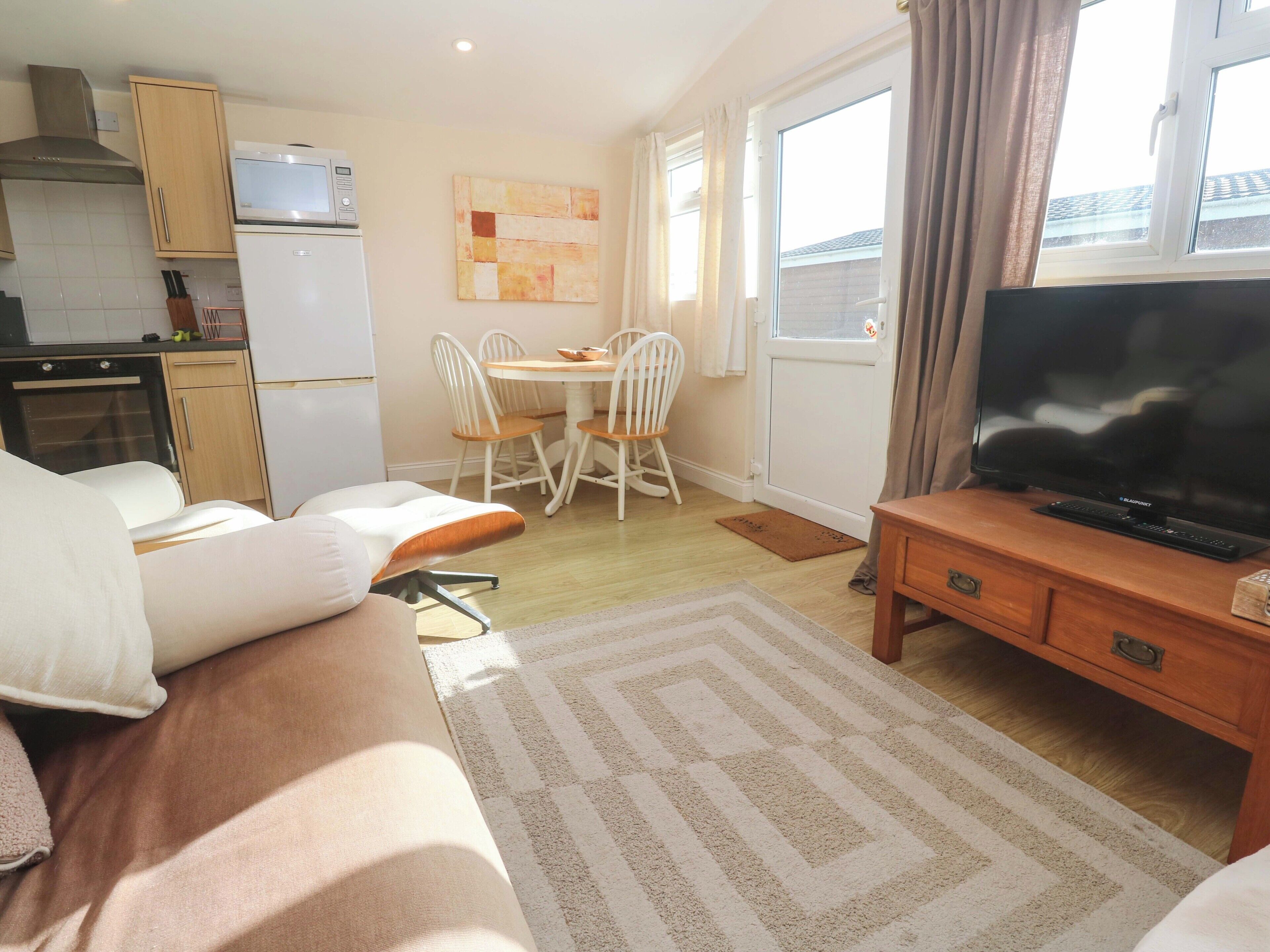 A compact living space with a kitchenette, a dining area, a sofa, a TV, and a window with curtains.