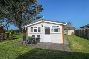Ein Bungalow mit Terrasse, einem kleinen Tisch mit Stühlen und einem eingezäunten Garten.