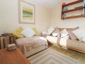 A living room with a sofa, a coffee table, a bookshelf, and a painting on the wall. - Chalet 225 (Padstow)