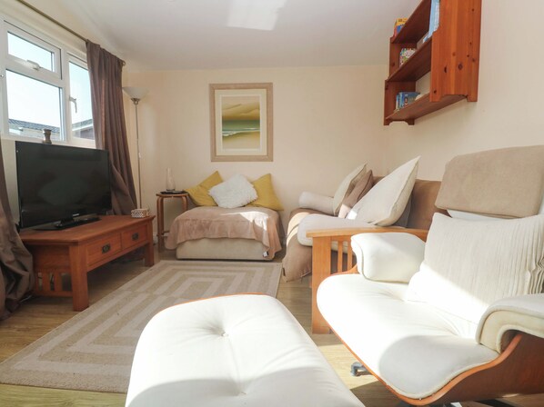 A living room with a television, sofa, armchair, and a painting on the wall. - Chalet 225 (Padstow)