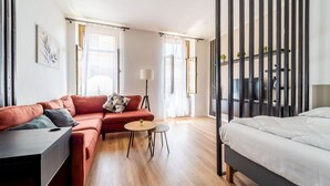 A modern hotel room with a red sofa, a small round table, a bed, and a large window with curtains. - GuestHost - Modern Flat X4 near the Center (Trieste)