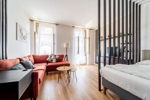 A modern hotel room with a sofa, a small round table, a bed, and a large window with curtains. - GuestHost - Modern Flat X4 near the Center (Trieste)