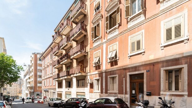 A street view with parked cars and a row of multi-story buildings with balconies. - GuestHost - Modern Flat X4 near the Center (Trieste)