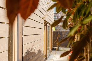 Ein schmaler Holzkorridor mit einer Tür und einem Fenster, der zu einem Balkon mit Blick auf ein Gebäude führt.