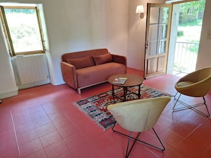 Ein Wohnzimmer mit einer Couch, einem kleinen runden Tisch, einem Sessel, einer Heizung und einer Tür, die nach draußen führt.