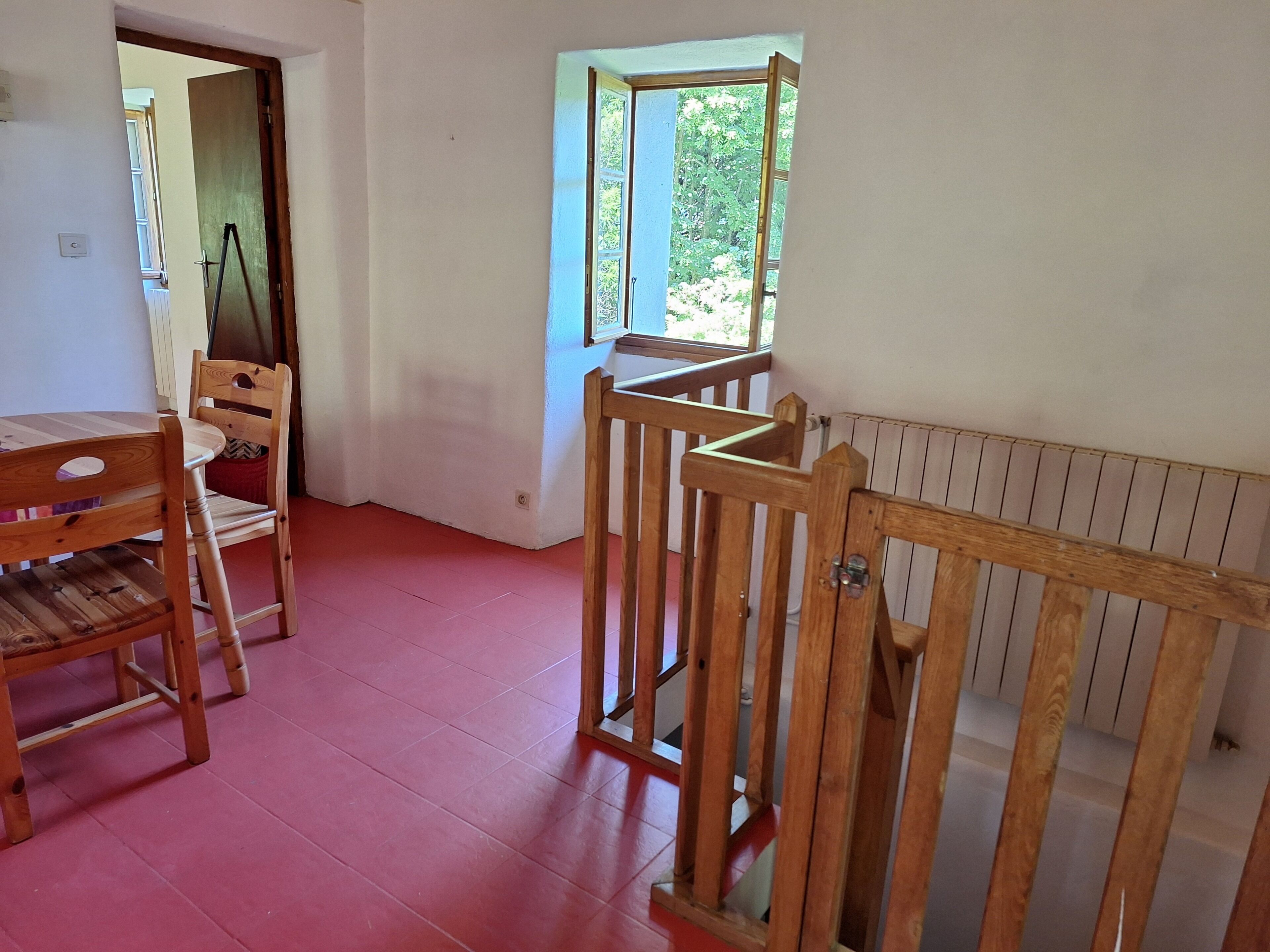 Een kamer met een houten stoel, een tafel, een raam met uitzicht op bomen, en een radiator.