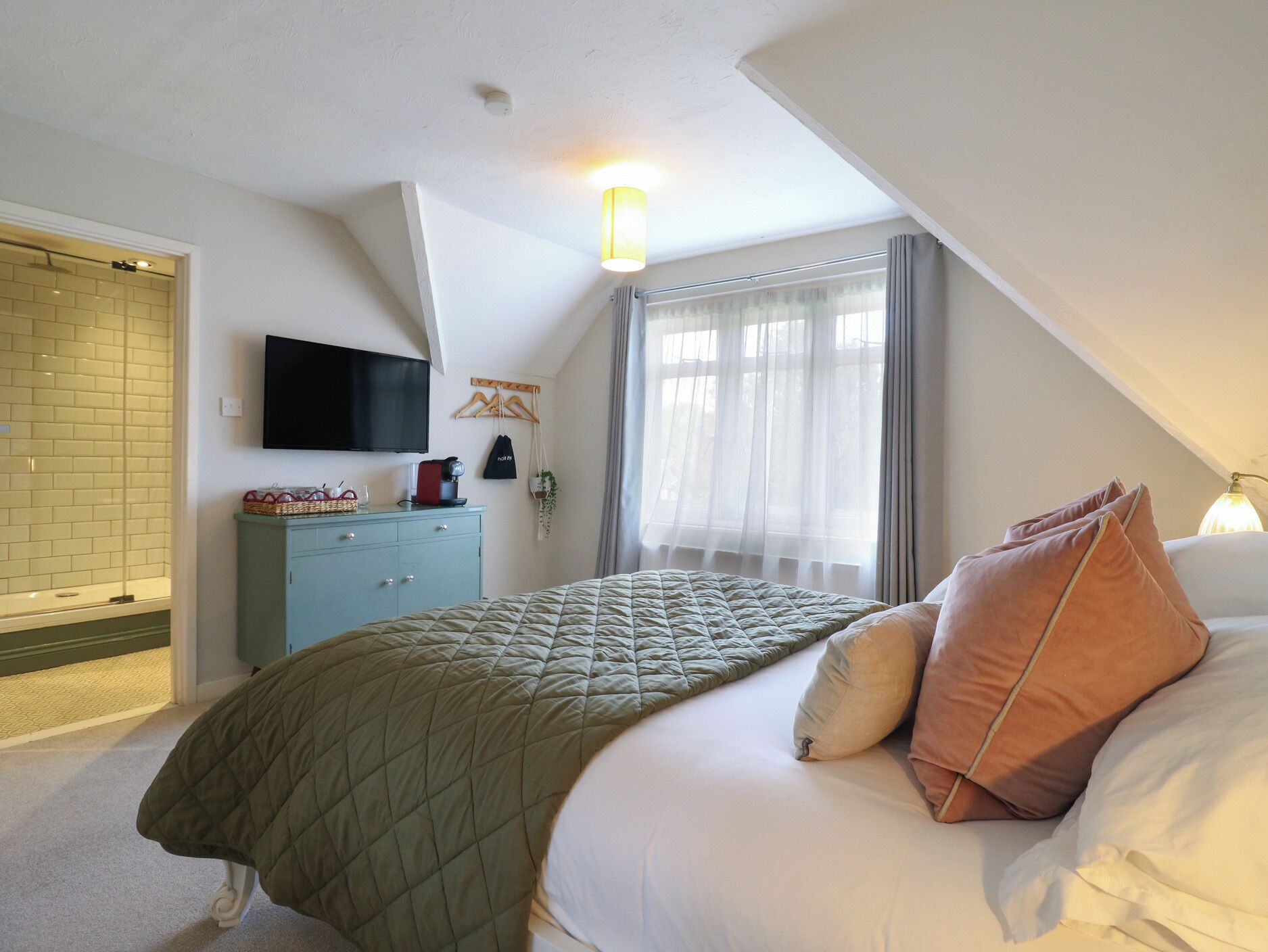 A bedroom with a bed, a TV, a dresser, and a window with curtains.