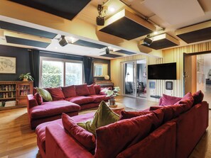 Un salón con un sofá rojo, una estantería, un televisor de pantalla plana y un ventanal corredero que da a un balcón.