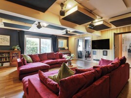 A living room with a red sofa, a bookshelf, a flat-screen TV, and a sliding glass door leading to a balcony.