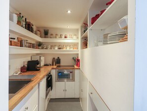 A compact kitchen with a microwave, oven, and various kitchen appliances. There are shelves with jars and kitchen utensils. - Denmark House (Chatham)