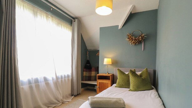 Een slaapkamer met een bed, kussens, een nachtkastje, een lamp, wanddecoratie en een raam met gordijnen.