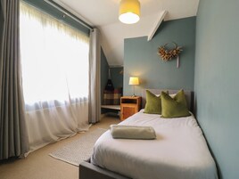 A bedroom with a bed, pillows, a nightstand, a lamp, a wall decoration, and a window with curtains.