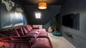 Een kamer met een grote wereldkaart, een donker plafond, een hanglamp, een televisietoestel en een comfortabele zithoek.