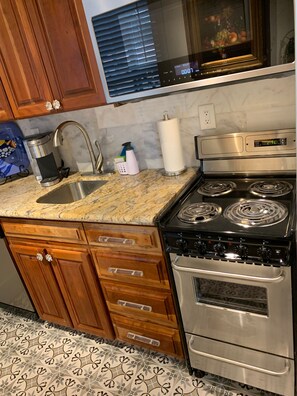 A kitchen with wooden cabinets, a stainless steel sink, a stove, and patterned floor tiles.