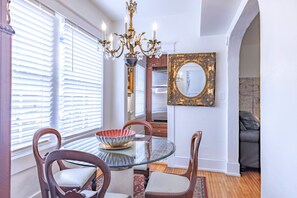 A dining area with a glass table, wooden chairs, a chandelier, and a mirror on the wall.