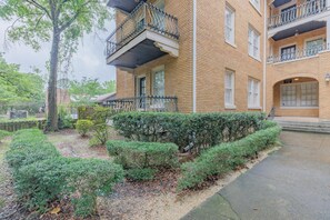 A multi-story brick building with balconies, a paved walkway, and well-maintained shrubbery.