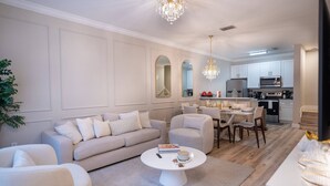 A modern living room with a sofa, armchairs, a dining table, and a kitchen in the background. - Disney 3BR Villa in Lucaya Harbor Resort (Kisssimmee)