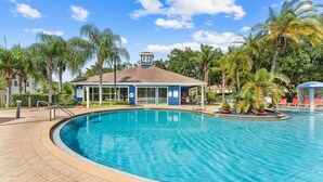 A swimming pool with a clear blue water, surrounded by palm trees and a building with a blue roof. - Disney 3BR Villa in Lucaya Harbor Resort (Kisssimmee)