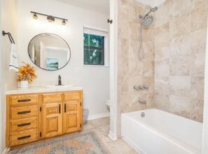 A bathroom with a wooden vanity, a round mirror, a shower with a handheld showerhead, and a bathtub. - Spacious Lake House-Hot Tub-Large Yard-Grill (Brownwood)