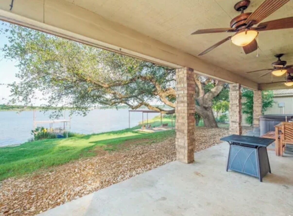 A covered patio with a view of a lake, a table, and a ceiling fan.