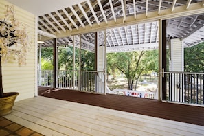 Eine überdachte Veranda mit Holzboden, Metallgeländer und großen Fenstern mit Blick auf einen Garten.