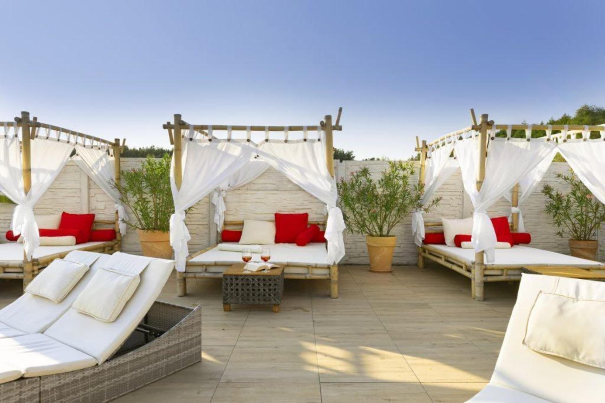 Une terrasse sur le toit dotée de quatre lits à baldaquin, chacun agrémenté de coussins rouges, et d’un canapé en osier avec des coussins.