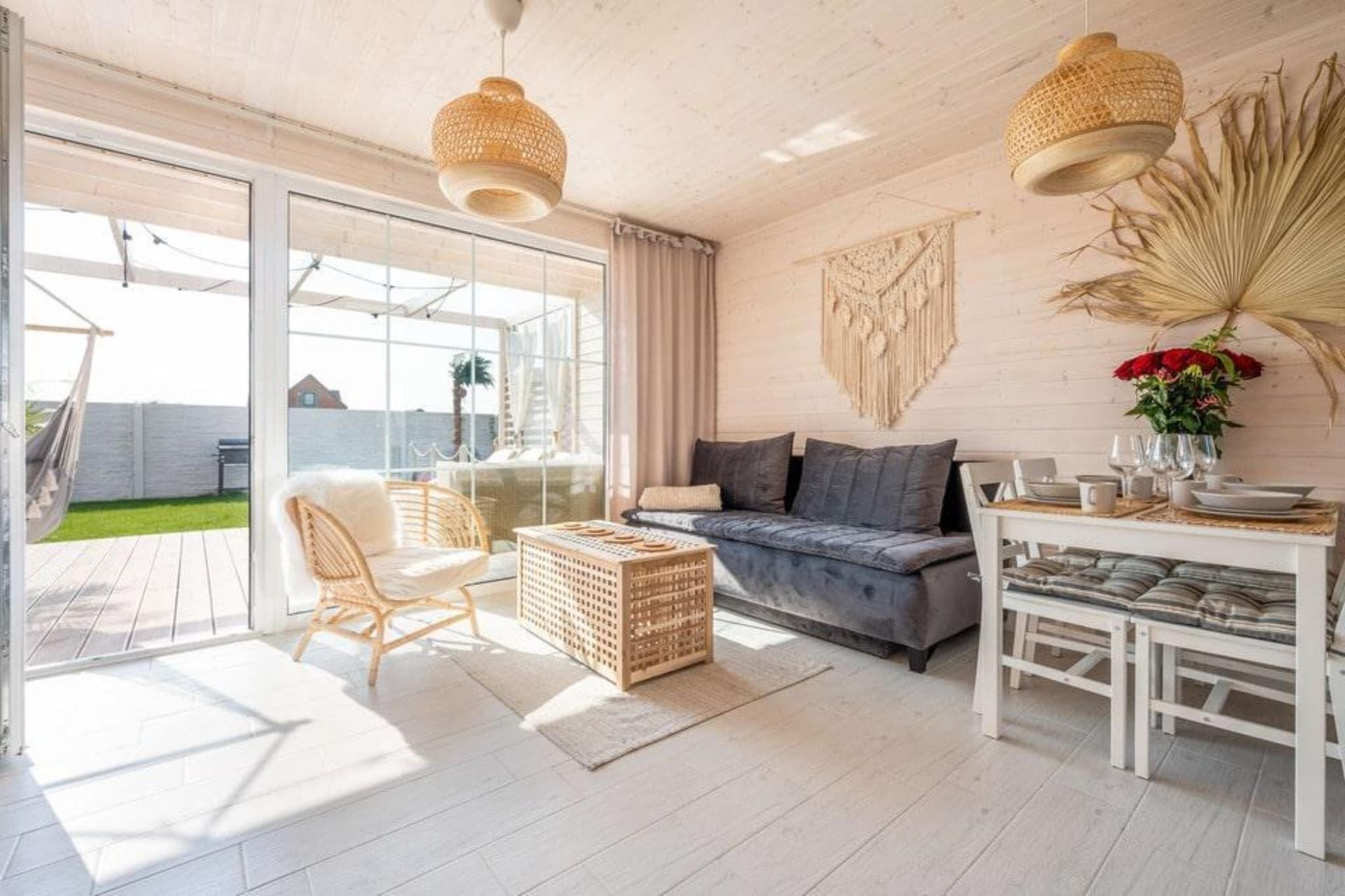 Amplia sala de estar con sofá, mesa de comedor, sillas de mimbre y un ventanal con vistas a un jardín.