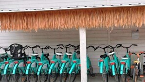 En rad cyklar parkerade under en konstruktion med ett halmtak.
