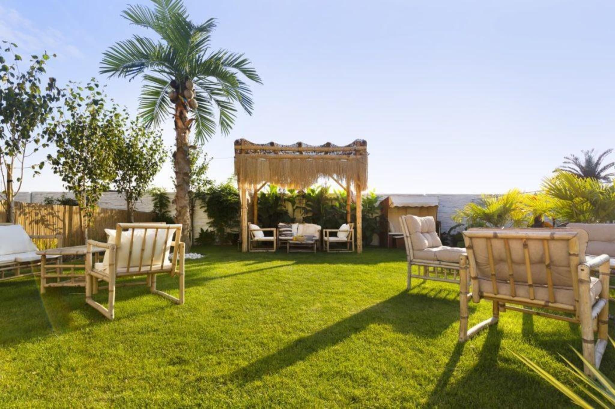 Une terrasse avec des meubles d’extérieur, un palmier et une structure recouverte de chaume.