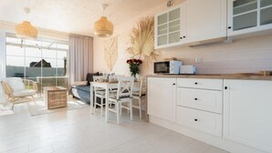 A modern kitchen with white cabinetry, a dining area with a table and chairs, and a large window providing natural light. - Holiday home with garden, air conditioning, pool (Kopan)