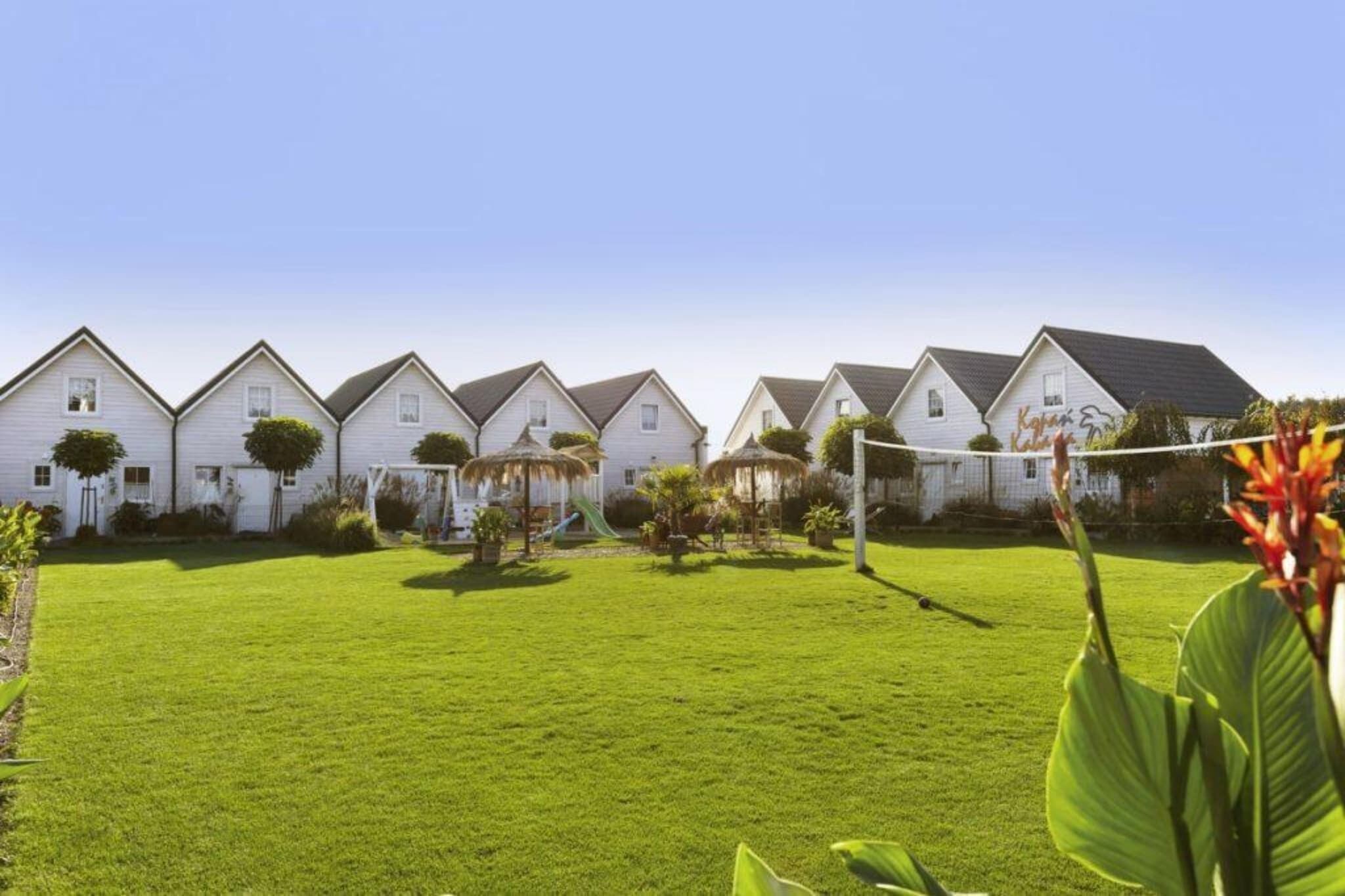 A row of white houses with a well-maintained lawn and a volleyball net in the foreground.