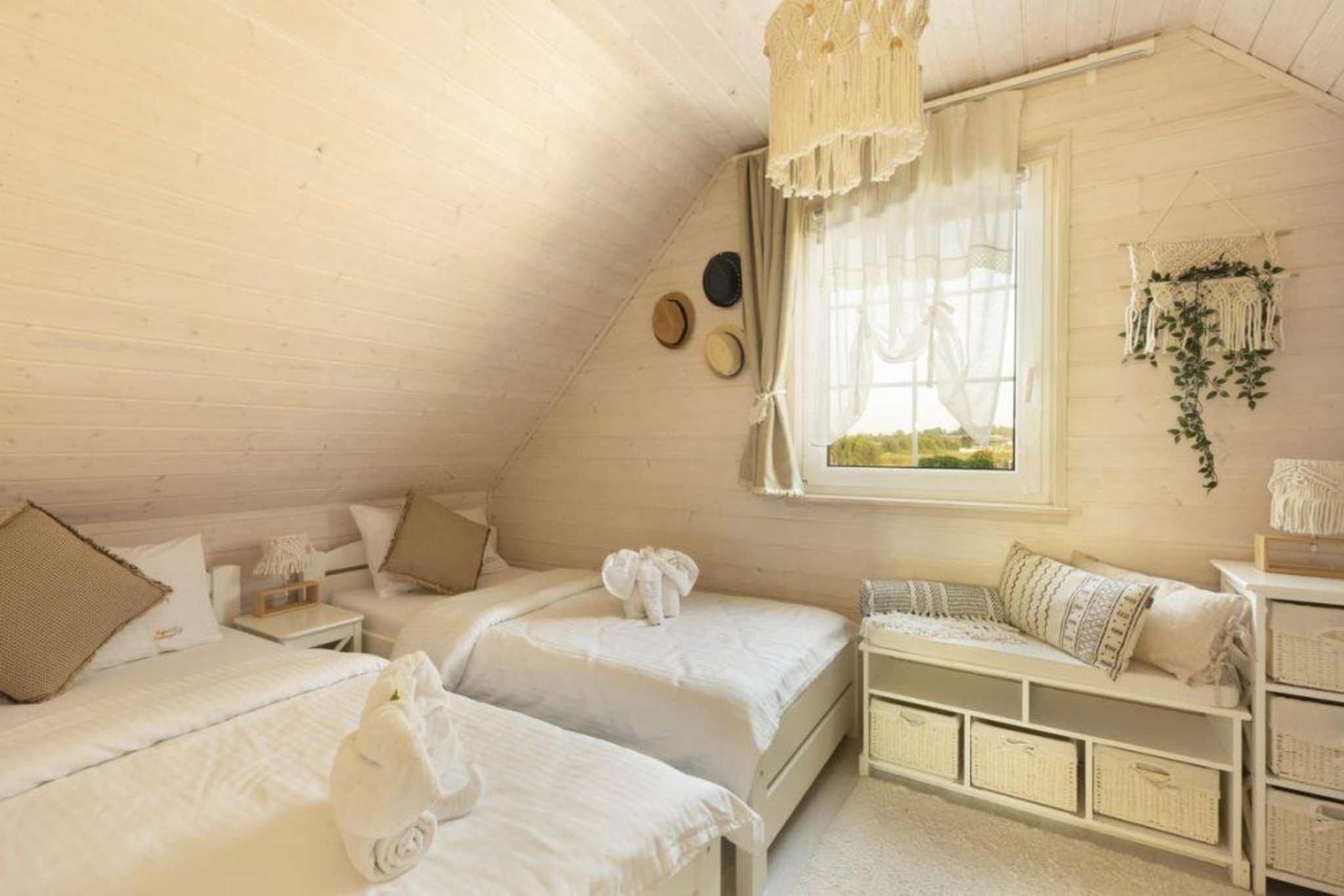 Une chambre mansardée agréable et bien éclairée, avec deux lits, une petite table et une fenêtre avec des rideaux.