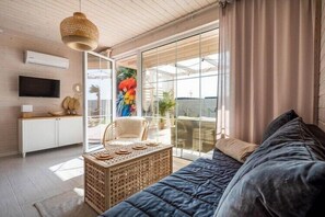 Ein modernes Wohnzimmer mit einer Couch, einem Fernseher, einem Korbtisch und einer großen Schiebeglastür, die zu einem Außenbereich führt.