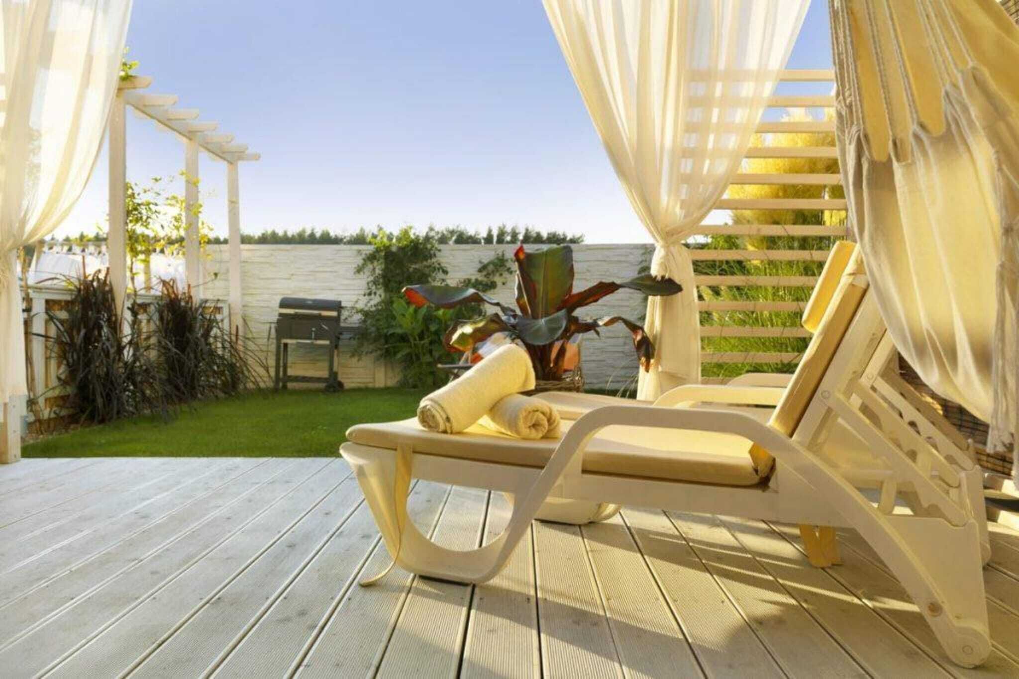 Une terrasse en bois surmontée d’un auvent blanc et dotée d’une chaise longue avec une serviette.
