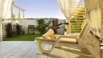 Une terrasse en bois surmontée d’un auvent blanc et dotée d’une chaise longue avec une serviette.