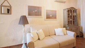 A living room with a sofa, a lamp, a cabinet, and two framed pictures on the wall. - Incanto Retreat with Terrace – Golfo Aranci (Punta Pedrosa)