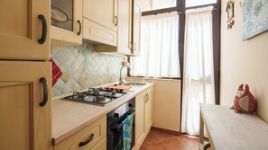 Eine Küche mit Holzschränken, einem Gasherd, einer Spüle und einem Fenster mit Vorhängen.