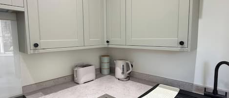 A kitchen with white cabinets, a black induction cooktop, a kettle, a toaster, and a sink.