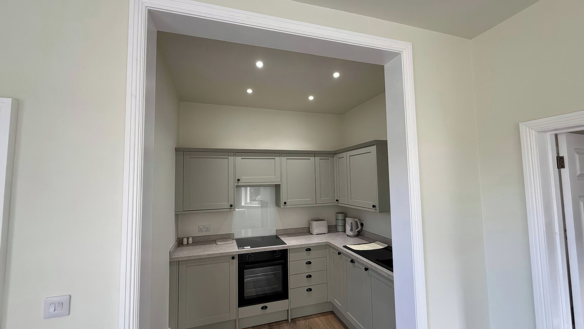 A compact kitchen with white cabinets, a built-in oven, and a countertop with a kettle and toaster.