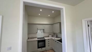 A compact kitchen with white cabinets, a built-in oven, and a countertop with a kettle and toaster.