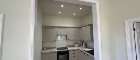 A compact kitchen with white cabinets, a built-in oven, and a countertop with a kettle and toaster.
