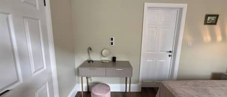 A bedroom with a bed, a bedside table with a lamp, a mirror, and a door.