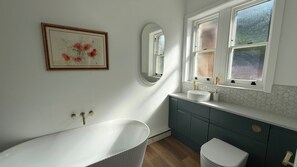 A bathroom with a freestanding tub, a sink with a hexagonal tile backsplash, a mirror, and a framed artwork on the wall. - Holt Hall - Ground Floor Apartment (Matlock)