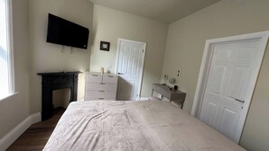 A bedroom with a bed, a dresser, a desk, a television, and a door. - Holt Hall - Ground Floor Apartment (Matlock)