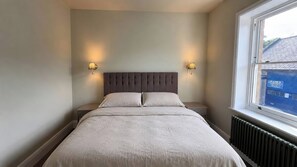 Ein Schlafzimmer mit einem Bett, zwei Nachttischlampen, einem Fenster und einer Heizung.