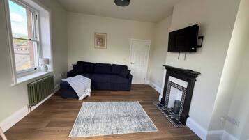 Ein Wohnzimmer mit einem dunkelblauen Sofa, einem gemusterten Teppich, einem Kamin und einem an der Wand befestigten Fernseher.